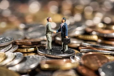 Small figures of two men shaking hands on a pile of coins. Stock Photos