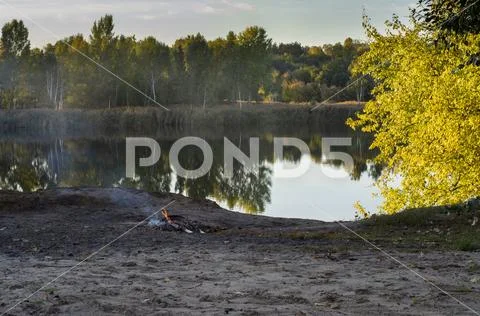 A small fire is burning on the shore of a beautiful lake. Stock Photos