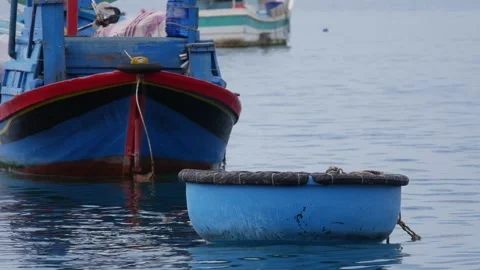 Small fishing boats float on calm water near the shore, with a blue boat in fron Видео 342334879