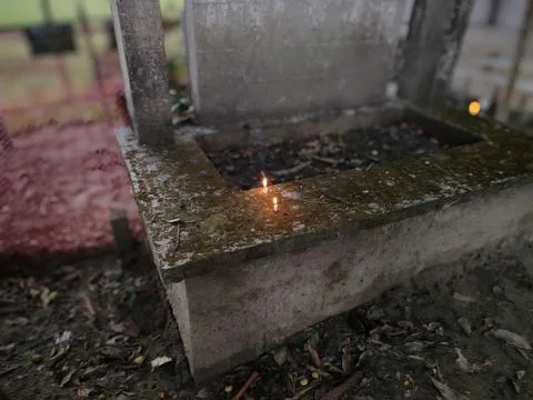 A small flame burns atop a moss-covered concrete structure with a rectangul.. Stock Photos