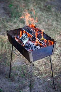 A small folding portable brazier filled with burning wood. Cooking on the gri Stock Photos