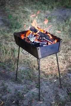 A small folding portable brazier filled with burning wood. Cooking on the gri Stock Photos