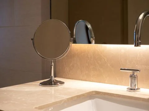 Small folding round makeup mirror standing near sink basin with marble top .. Stock Photos