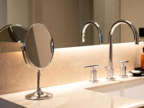 Small folding round makeup mirror standing near sink basin with marble top .. Stock Photos