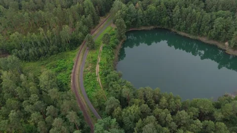 Small forest lake ringed by trees and a curving track 스톡 동영상 340646723