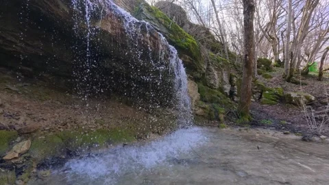 Small forest waterfall cascading over mossy rocks in spring, natural woodland st Stock Footage 330120575
