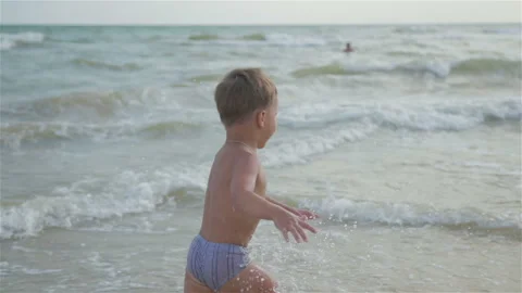 Small, frisky, happy boy, son swimming in the sea. He runs and jumps and Vídeos de archivo 93716384