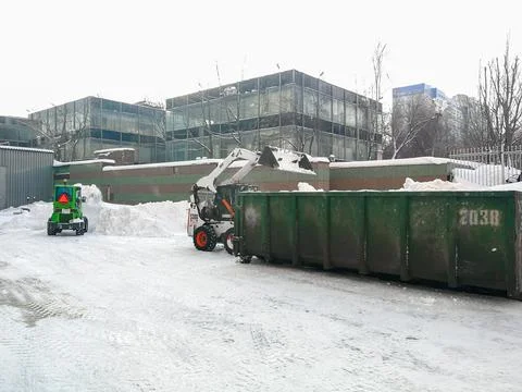 Small front-end loaders clear snow from the street and load into a bunker. Stock Photos