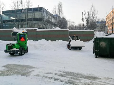 Small front-end loaders clear snow from the street and load into a bunker. Stock Photos