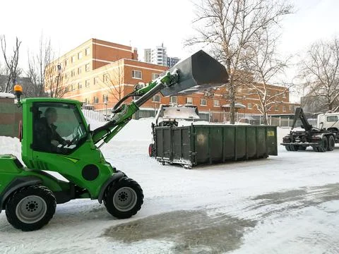 Small front-end loaders clear snow from the street and load into a bunker. Stock Photos