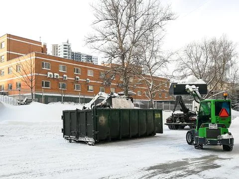 Small front-end loaders clear snow from the street and load into a bunker. Stock Photos
