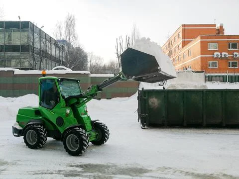 Small front-end loaders clear snow from the street and load into a bunker. Stock Photos