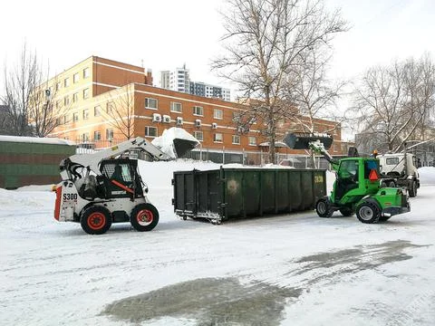 Small front-end loaders clear snow from the street and load into a bunker. Stock Photos