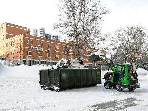 Small front-end loaders clear snow from the street and load into a bunker. Stock Photos