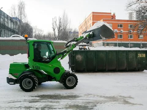 Small front-end loaders clear snow from the street and load into a bunker. Stock Photos