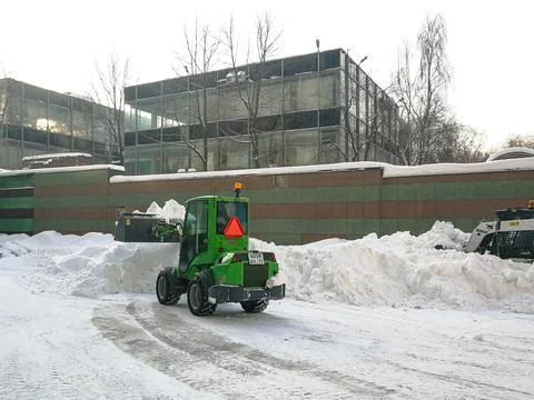 Small front-end loaders clear snow from the street and load into a bunker. Stock Photos