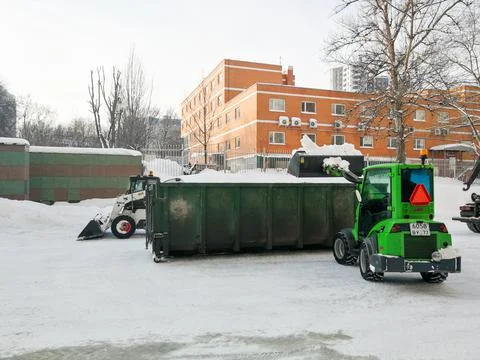 Small front-end loaders clear snow from the street and load into a bunker. Stock Photos