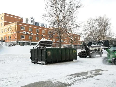 Small front-end loaders clear snow from the street and load into a bunker. Stock Photos