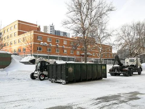 Small front-end loaders clear snow from the street and load into a bunker. Stock Photos