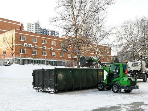 Small front-end loaders clear snow from the street and load into a bunker. Stock Photos