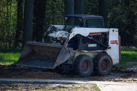 A small front loader clears the ground after construction work in a city park Stock Photos