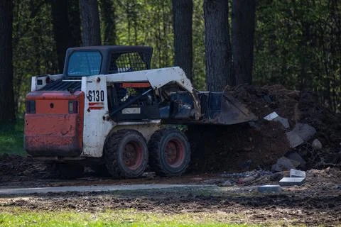 A small front loader picks up rubbish after construction work in a city park. Stock Photos