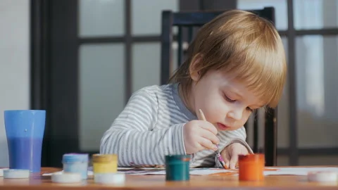A small funny child of 2-3 years old drawing using paints and brushes, sitting Stock Footage 151108956