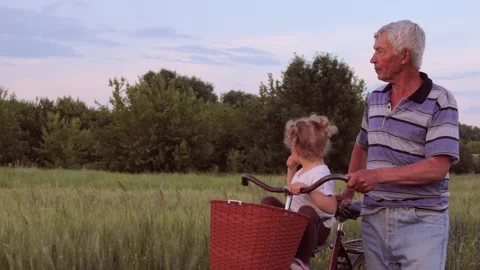 Small funny kid riding with her grandfather on green field against blue sky Stock Footage 291394706
