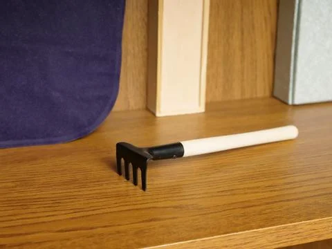 Small garden hand rake with handle on shelf. Tool for plant and soil care. Photos