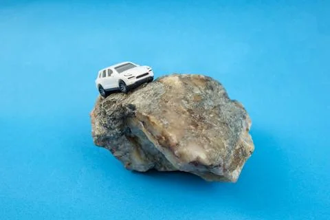 Small generic suv model car climbing a rock in balance on blue background Foto stock