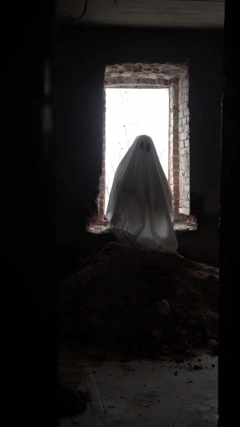 Small ghost in classic sheet stands quietly in ruined room, window and mound Stock Footage 320248236