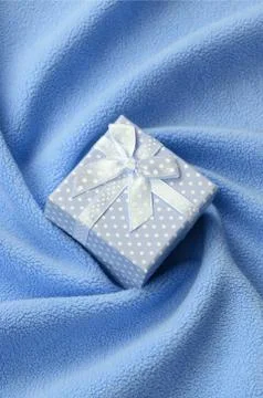 A small gift box in blue with a small bow lies on a blanket of soft and furry Stock Photos
