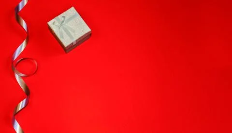 Small gift box with decor of gift blue ribbon on a red background. Space for Stock Photos