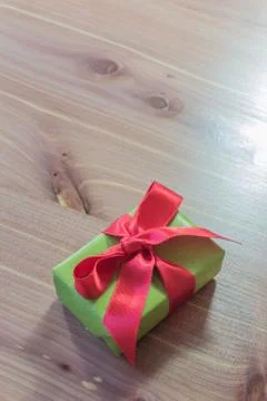 Small gift box, green with large red satin ribbon, diagonal, neutral wood Stock Photos