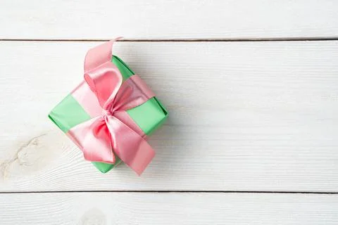 A small gift box in green packaging with a pink ribbon on a white wooden Stock Photos