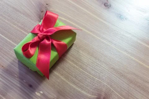 Small gift, diagonal on a wood table, wrapped in green with big red satin bow Stock Photos