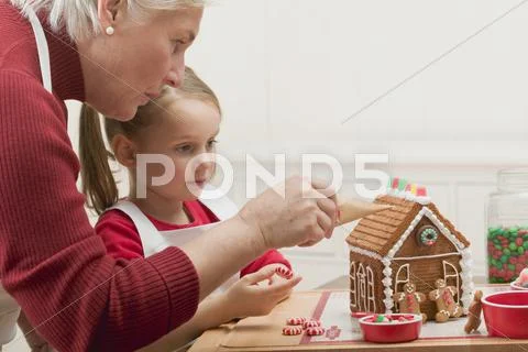 Small Girl And Grandmother Decorating Gingerbread House