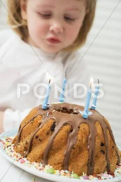 Small Girl Blowing Out Candles On Birthday Cake