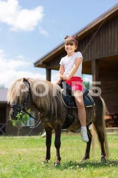 Small girl with cute hairstyle sitting on the horse and smiling Stock Photos