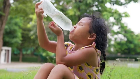 Small girl drinking iced cold water from disposable bottle at park. Stockbeeldmateriaal 202173248