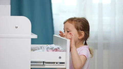 Small girl pulls open white dresser drawer with baby clothes Stock Footage 330102619