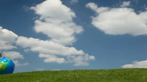 Small girl rolling inflatable globe looking ball on meadow Stock Footage 1106066