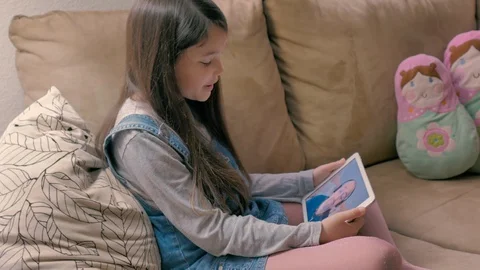 Small girl sitting on the couch talks happily with her father through a tablet Stock Footage 128671698