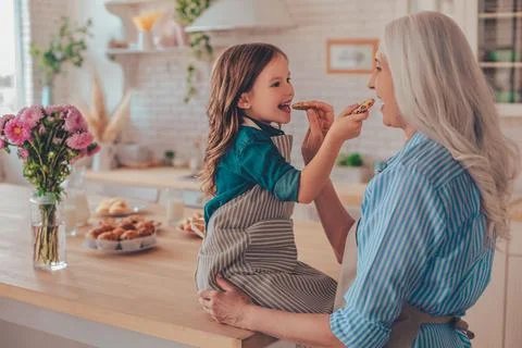 Small girl sitting on the kitchen table and feeding grandmother with biscuits Stock Photos