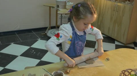 A Small Girl is Trying to Roll Out the Clay Using a Round Wooden Stick to Make Stock Footage 59122666