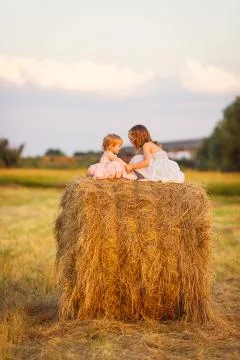 Small girls sit on haystack wheat field sunset Stock Photos