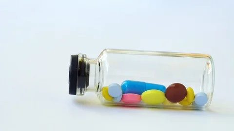 A small glass bottle with multi-colored pills and capsules rolls out of frame. Video stock 108673235