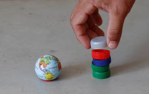 Small globe and hand stacking pet bottle tops representing plastic pollution and 库存照片