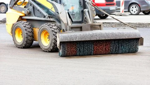 A small grader with a trailed nylon brush with hydraulics cleans the repaired Stock Photos