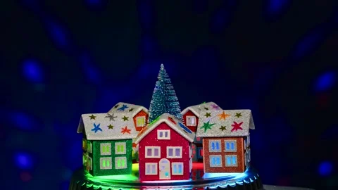 A small green Christmas tree rotates surrounded by five Christmas houses Stock Footage 291833556